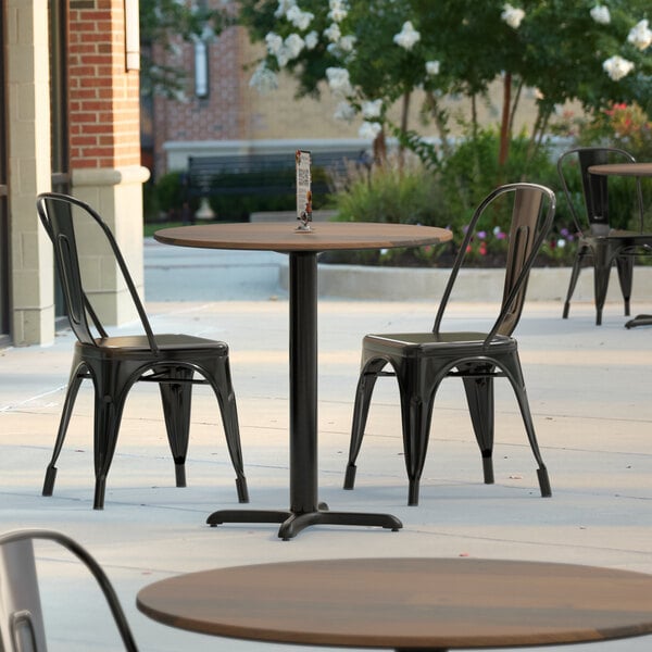 A Lancaster Table & Seating Excalibur round dining table with a textured farmhouse finish and cross base plate on a patio.