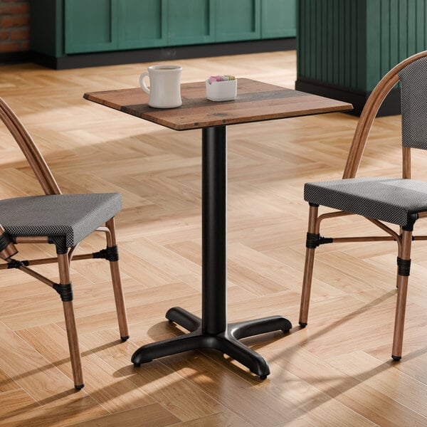 A square standard height table with a textured farmhouse finish and a black cross base plate, accompanied by two chairs.
