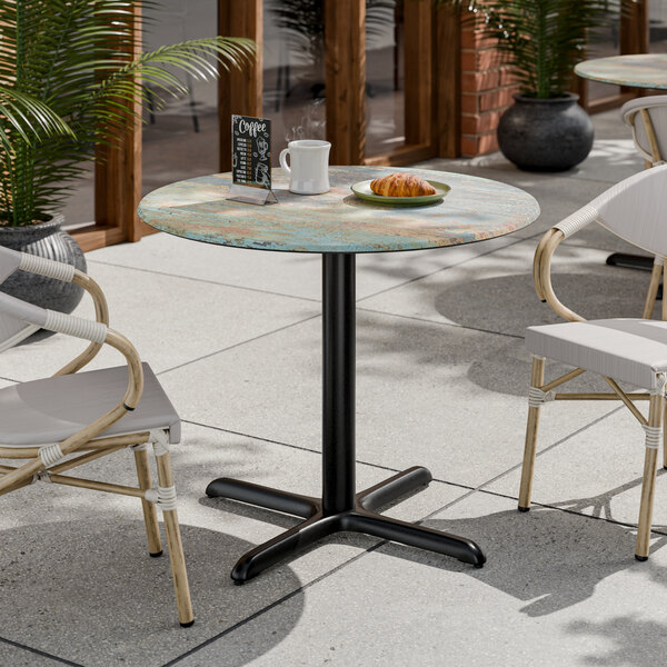 A round standard height table with a textured canyon painted faux metal finish and a black cross base plate.