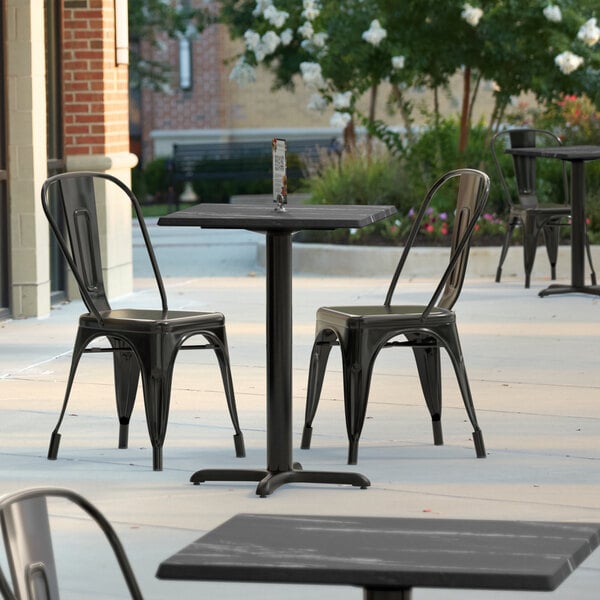 A Lancaster Table & Seating Excalibur square dining table with a black metal cross base on an outdoor patio.