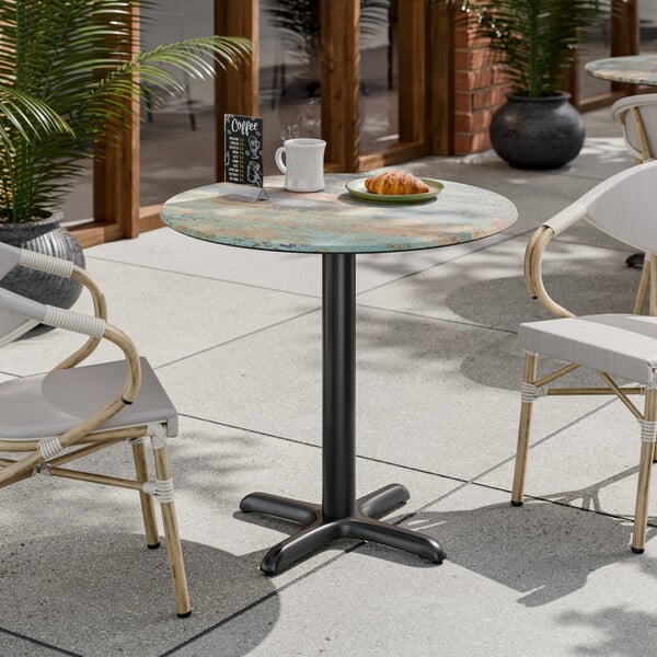 A round standard height table with a textured canyon painted faux metal finish and a cross base plate.