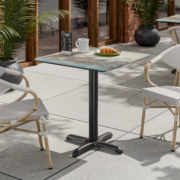 A square standard height table with a textured canyon painted faux metal finish and a cross base plate.