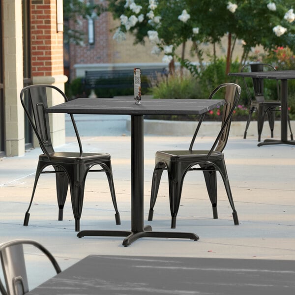 A Lancaster Table & Seating square dining table with a cross base on an outdoor patio.