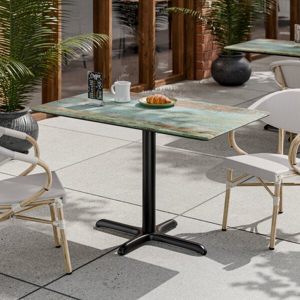 A rectangular standard height table with a textured canyon painted faux metal finish and a black cross base plate.