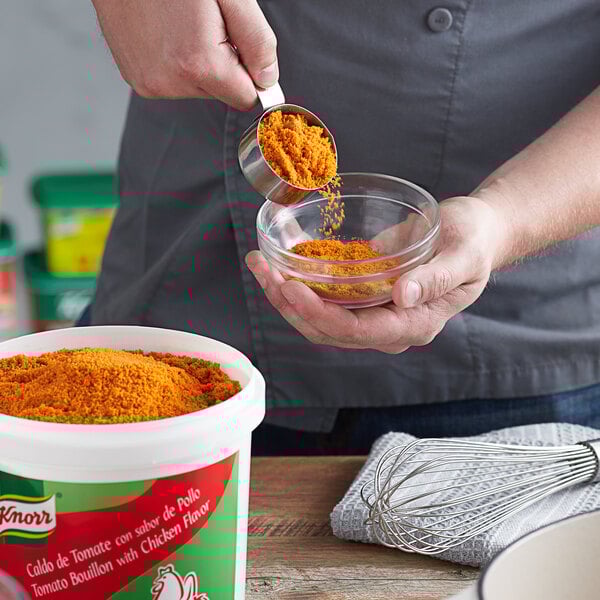 A person mixing Knorr Caldo de Tomate con sabor de Pollo into food in a bowl.