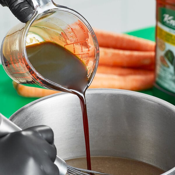 A person pouring Knorr Ultimate Liquid Concentrated Beef Base into a bowl of carrots.