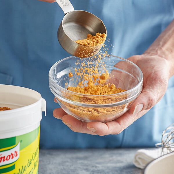 A person pouring yellow Knorr shrimp bouillon powder into a bowl.