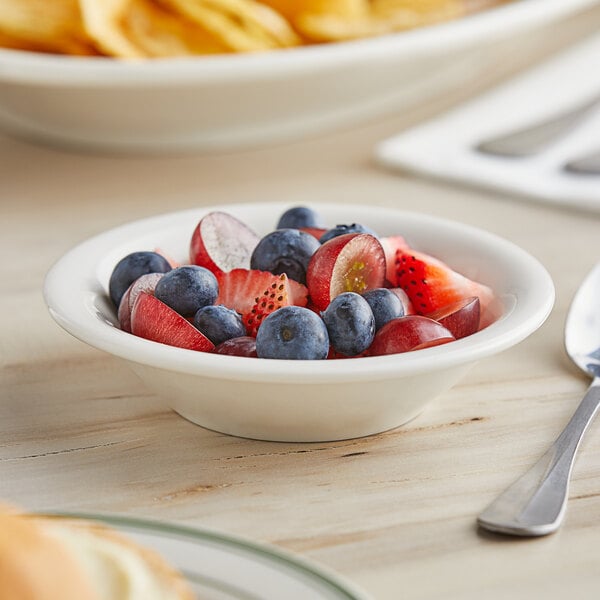 A Tuxton Reno eggshell china fruit bowl filled with fruit on a table.
