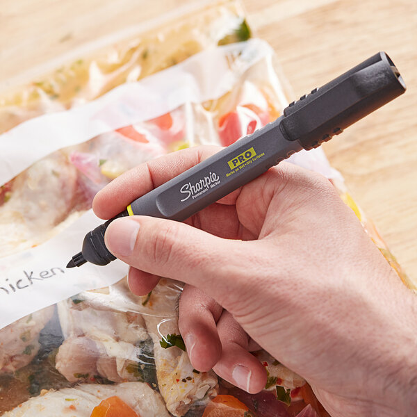 A hand using a Sharpie marker to write on a plastic bag of food.