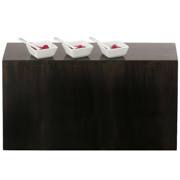 A black wooden table with a row of Cal-Mil Midnight Plate Risers holding white bowls of food with raspberries and spoons.