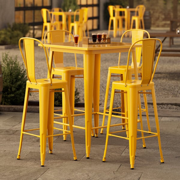 A Lancaster Table & Seating citrine yellow bar height table with 4 yellow chairs on an outdoor patio.