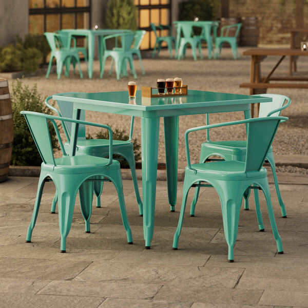 A Lancaster Table & Seating outdoor table in aquamarine with four green plastic chairs.