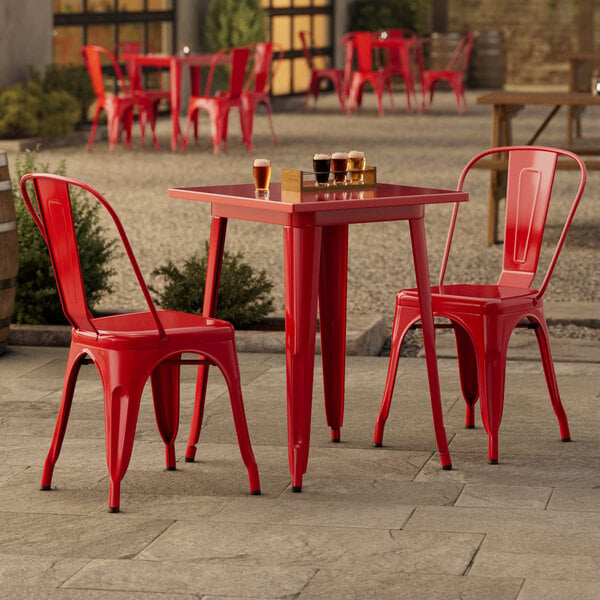 A Lancaster Table & Seating ruby red metal table and chairs outside on a stone patio.