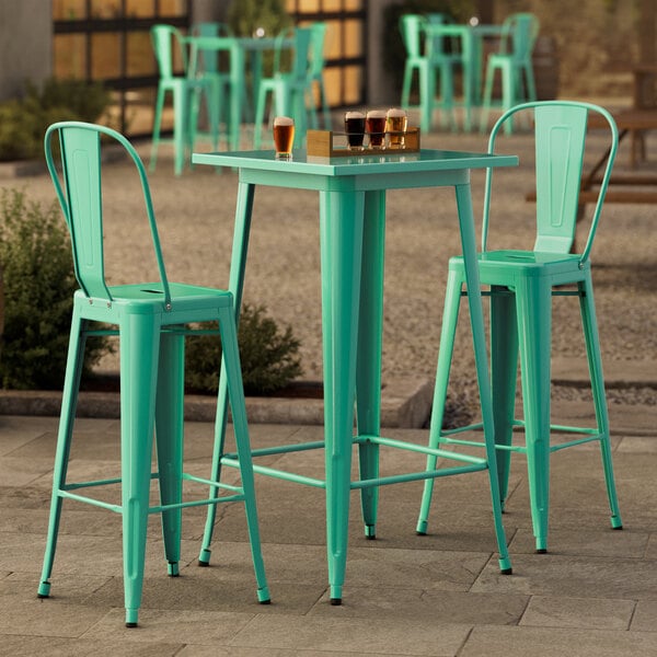 A Lancaster Table & Seating aquamarine bar height outdoor table with two green metal barstools.