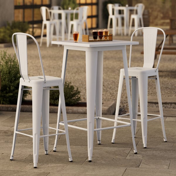 A Lancaster Table & Seating pearl white bar height outdoor table with 2 cafe barstools.