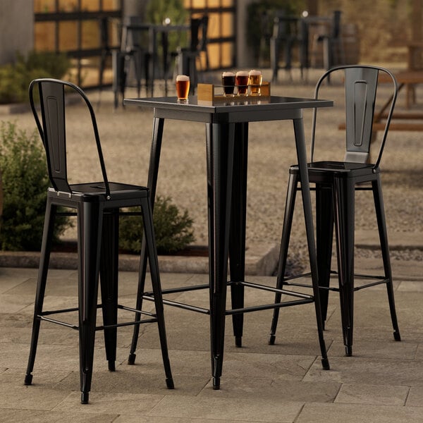 A Lancaster Table & Seating black bar table with two black chairs on a patio.