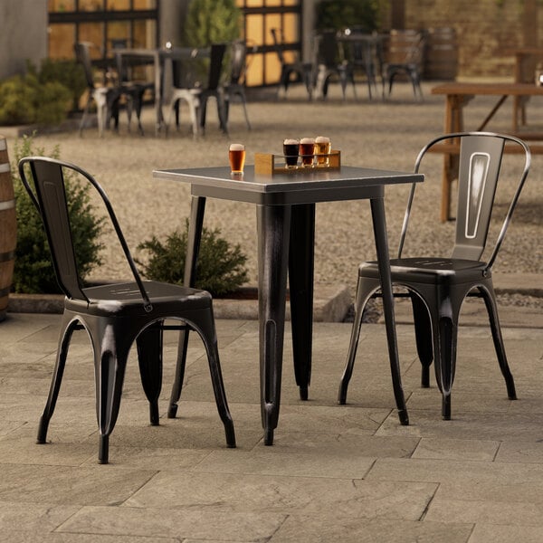 A Lancaster Table & Seating outdoor table with two black chairs on a patio.