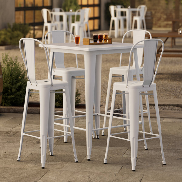 A Lancaster Table & Seating Pearl White bar height outdoor table with 4 white chairs on a patio.