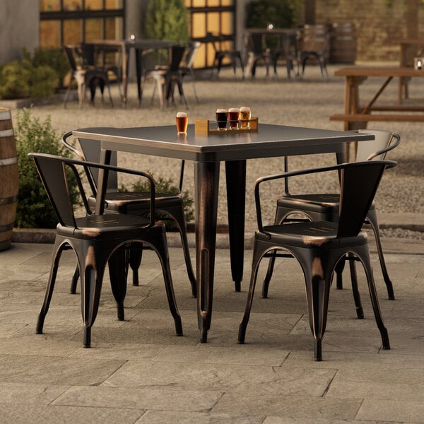 A Lancaster Table & Seating distressed copper outdoor table with chairs on a patio.