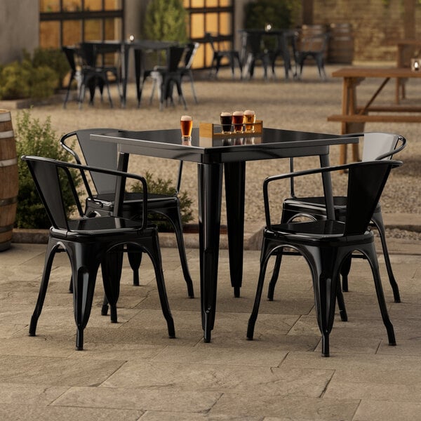 A Lancaster Table & Seating black metal table with four black chairs on an outdoor stone patio.