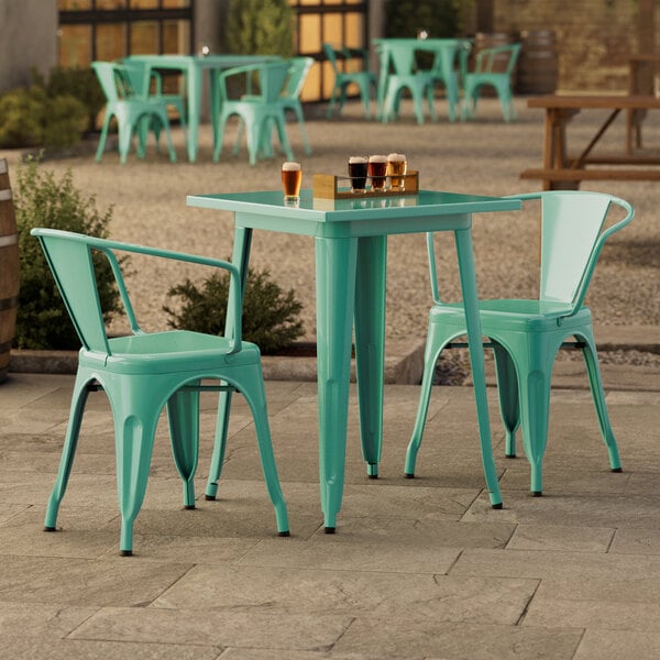 A Lancaster Table & Seating outdoor table in aquamarine with green chairs on a concrete patio.
