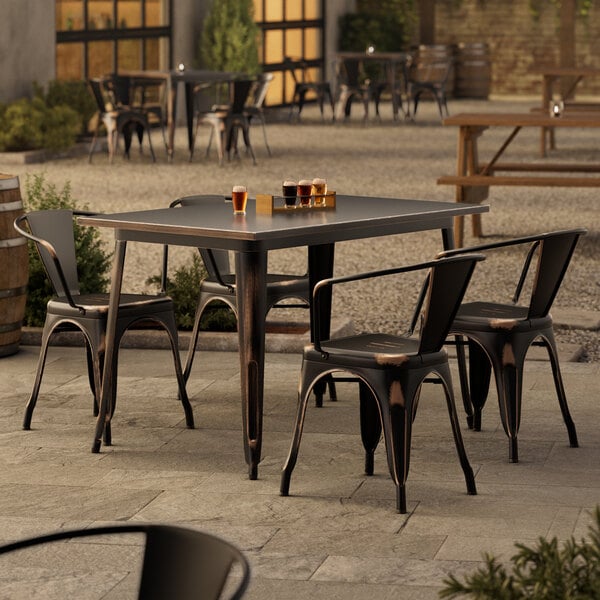 A Lancaster Table & Seating distressed copper table and chairs on an outdoor patio.