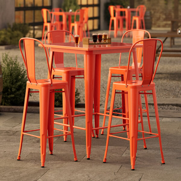 A Lancaster Table & Seating amber orange table with barstools on an outdoor patio.