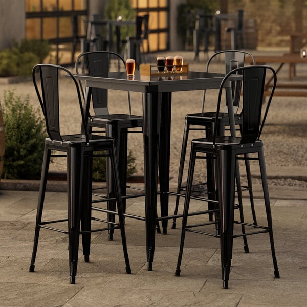 A black Lancaster Table & Seating bar table with four black chairs on a patio.