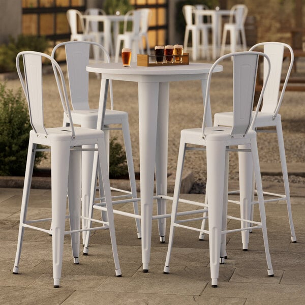 A Lancaster Table & Seating pearl white bar height table with four white bar stools on a patio.