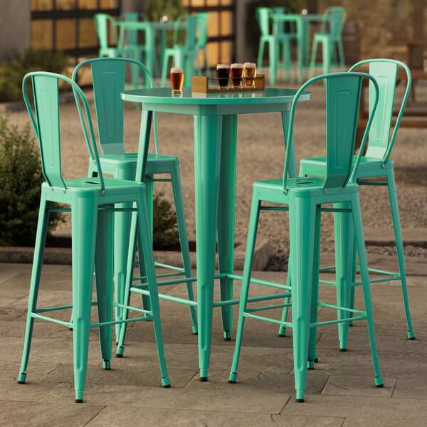 A Lancaster Table & Seating bar height outdoor table with aquamarine top and 4 green wire chairs.