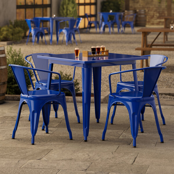 A Lancaster Table & Seating blue metal table with four chairs on an outdoor patio.