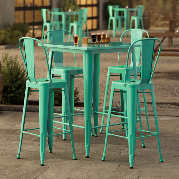 A Lancaster Table & Seating aquamarine bar height table with four green chairs on a patio.