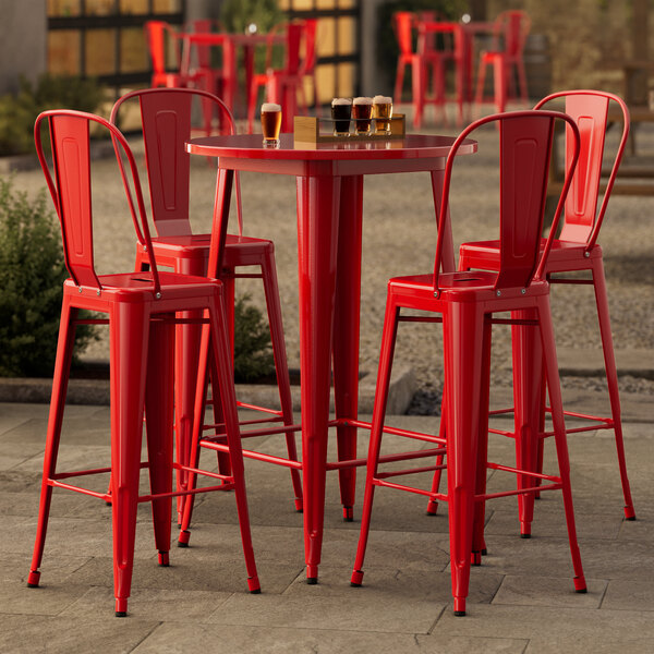 A Lancaster Table & Seating ruby red metal bar height table and chairs on an outdoor patio.