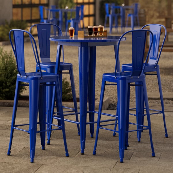 A Lancaster Table & Seating blue metal bar table with four blue chairs on an outdoor patio.