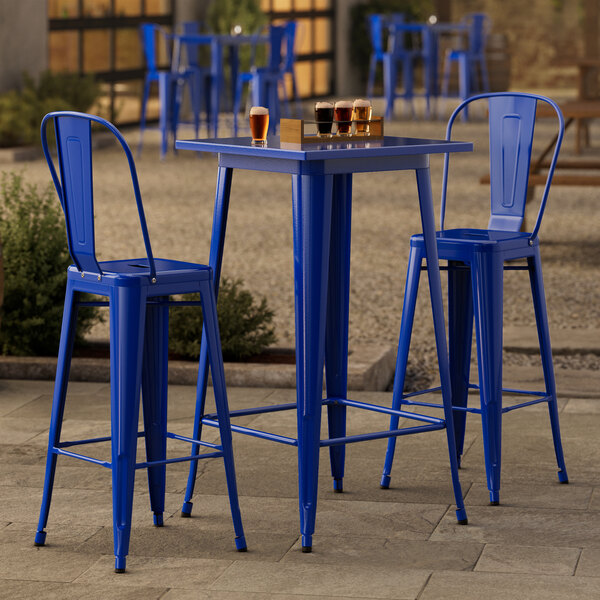 A Lancaster Table & Seating blue metal bar table with two blue bar stools on an outdoor patio.