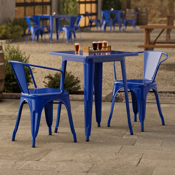 A Lancaster Table & Seating blue metal table and chairs on an outdoor patio.