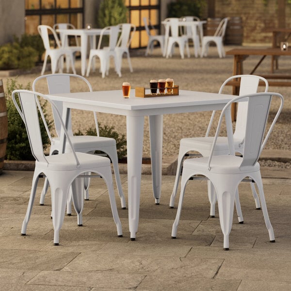 A Lancaster Table & Seating pearl white table with four white chairs on an outdoor patio.