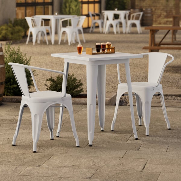 A white Lancaster Table & Seating outdoor table and chairs on a patio.