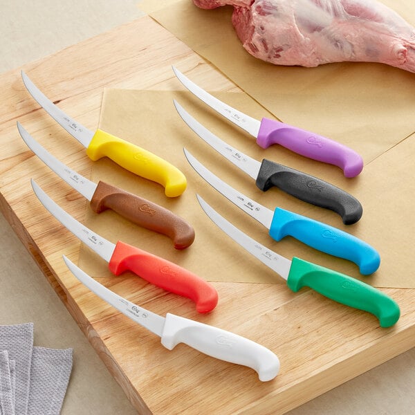 Choice 6" Curved Stiff Boning Knife with Yellow Handle next to a group of knives with different colored handles on a cutting board.