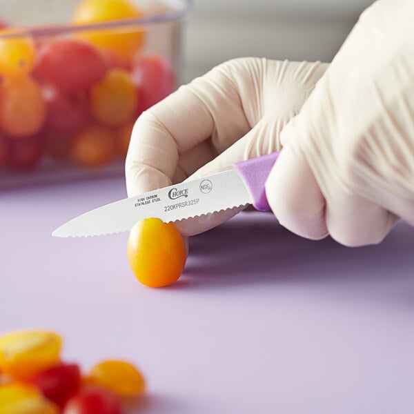 A person in gloves using a Choice serrated paring knife to cut a tomato.