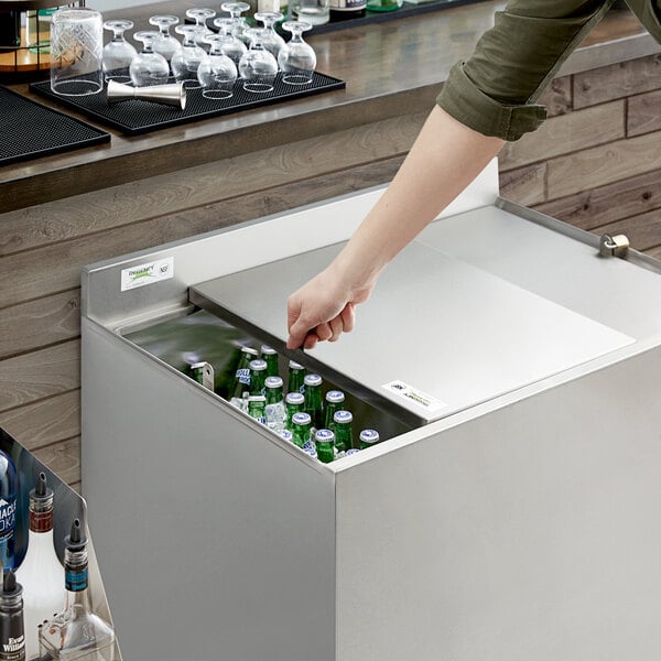 A hand using a black key to unlock a Regency Beer Box lid to put a glass bottle inside.