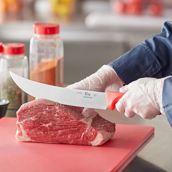 A person in gloves using a Choice cimeter knife to cut meat on a cutting board.