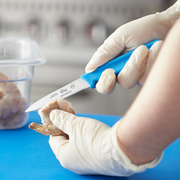 A person holding a Choice smooth edge paring knife with a blue handle to peel a piece of food.