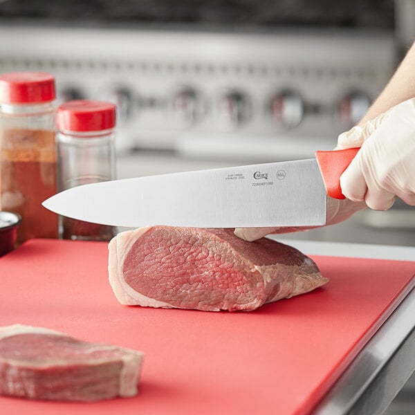 A person using a Choice 10" chef knife to cut raw meat on a red cutting board.