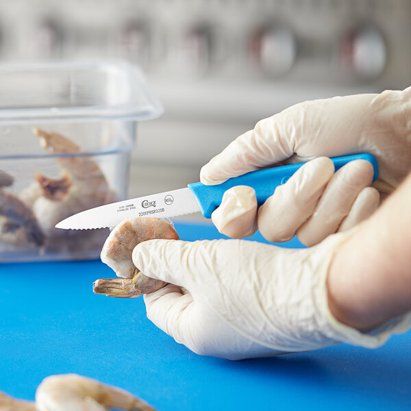 A gloved hand uses a Choice serrated paring knife to cut food.