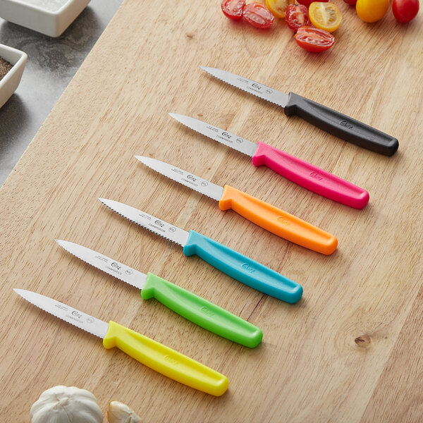 A group of Choice serrated paring knives with neon blue handles on a cutting board.