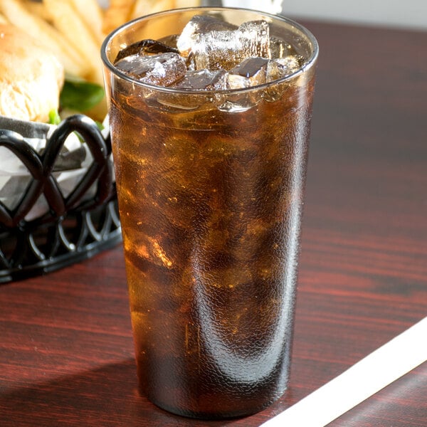 A Cambro amber plastic tumbler filled with brown liquid and ice on a table with a basket of food.