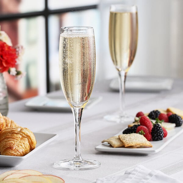 A close-up of a Nude Primeur flute of champagne and fruit on a table.