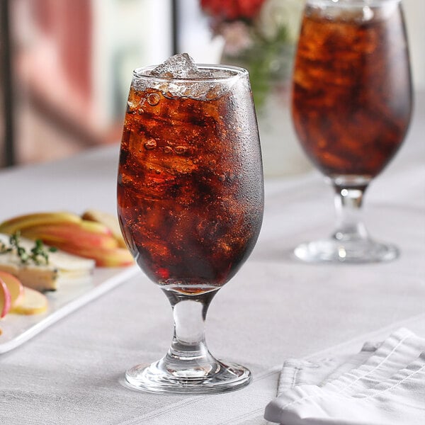 A Pasabahce Maldive stemmed beer glass filled with brown liquid and ice on a table.