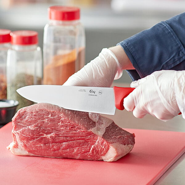 A person cutting raw meat with a Choice 8" Chef Knife with a red handle.